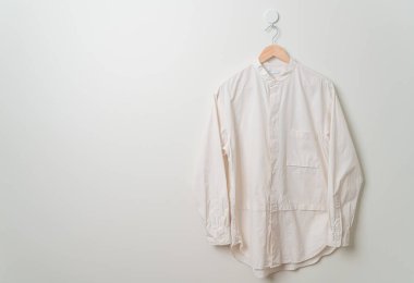 Duvarında ahşap askı olan bej bir gömlek asıyor.