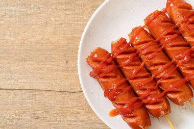 Beyaz tabakta ketçaplı kızarmış sosis şişi.