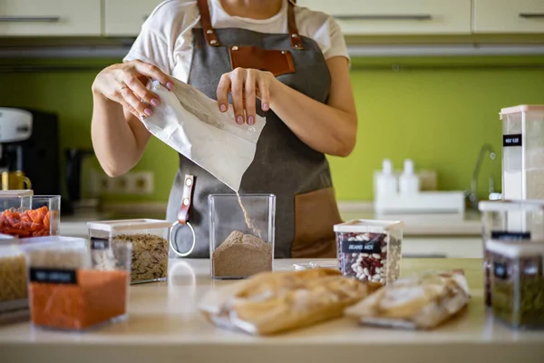 女性は透明な箱に健康なエンドウ豆のパスタを加える。台所の収納組織. — ストック写真