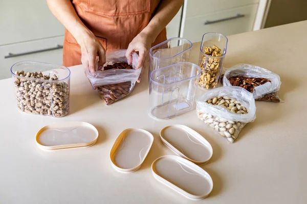 Крупный план домохозяйка руки положить орехи пластиковый пакет в контейнер коробку на деревянный стол на кухне — стоковое фото