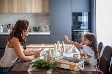Küçük kız Noel ağacı konisi yapıyor ve düğmelerle, ipliklerle süsleme yapıyor.