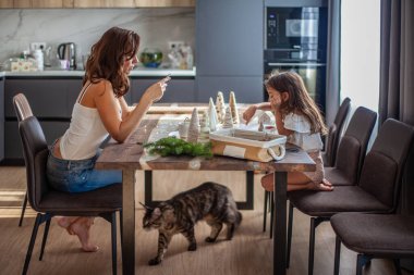 Küçük kız Noel ağacı konisi yapıyor ve düğmelerle, ipliklerle süsleme yapıyor.