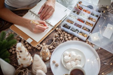 Genç bayanın en iyi görüntüsü, 2021 yılbaşı için yılbaşı ağacının olduğu masaya hedefler yazmak.