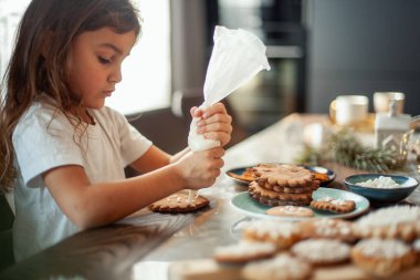 Küçük tatlı kız zencefilli ekmeği şekerle süslüyor. Noel konseptine hazırlık.