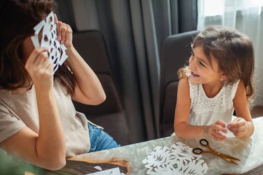 Küçük tatlı kız ve genç güzel kadın beyaz kağıttan kar taneleri kesiyor. Zencefilli ekmek ve marşmelovlu kakao..
