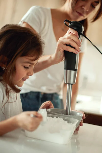 Mom and daughter prepare icing for gingerbread in their home kitchen. Beat with a blender. The girl helps the woman. — Stock Photo, Image
