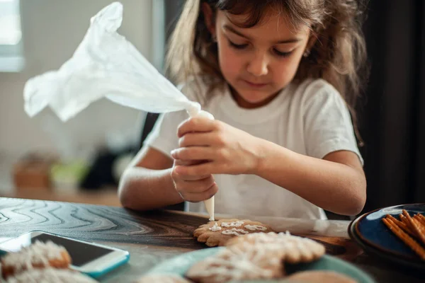 Mãe e crianças decorar pão de gengibre de Natal em casa. Um rapaz e uma rapariga pintam com cornetas com cobertura de açúcar em bolachas. Decoração de Ano Novo, ramos de uma árvore de Natal. — Fotografia de Stock