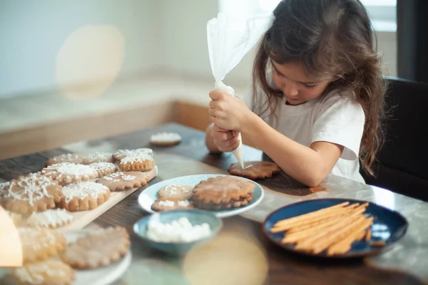 Little cute girl decorates gingerbread with sugar icing. Preparation for Christmas concept. — Stock Photo, Image