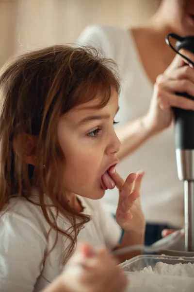 Mamãe e filha preparam a cereja para o pão de gengibre em sua cozinha doméstica. Bata com um liquidificador. A menina ajuda a mulher. — Fotografia de Stock