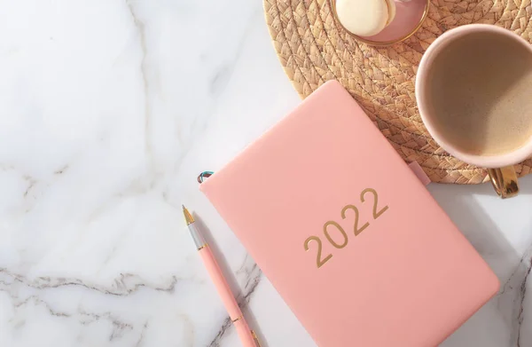 Rosa korall färgad dagbok för år 2022, penna, kaffe, makaron kaka på halm vävd underlägg — Stockfoto