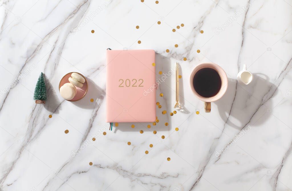 Flat lay composition with New Years decoration, coral colored 2022 diary book and coffee cup and Macaron cookie