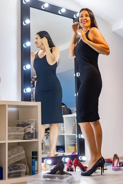 Módní brunetka žena výběru náušnice při pohledu na zrcadlo chystá na party událost — Stock fotografie