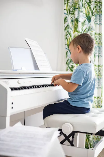 Netter kleiner Junge spielt weißes elektrisches Forte-Klavier und drückt Tasten Kind studiert an der Musikschule — Stockfoto