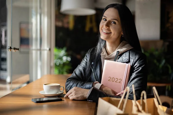 Ispirato giovane donna con un sorriso guardando attraverso la finestra e tenendo il diario color corallo 2022 — Foto Stock