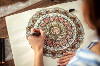 Uzun saçlı güzel bir kız dairesel bir mandala deseni çiziyor..