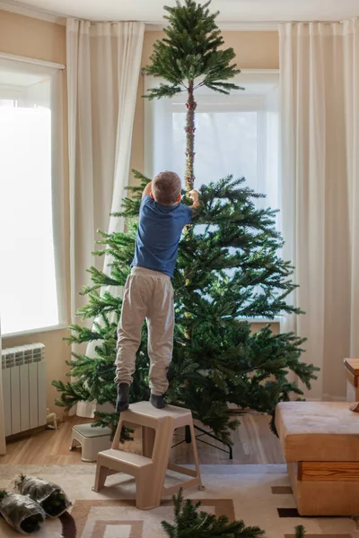 少年は自宅のリビングルームで人工的なクリスマスツリーを収集します — ストック写真