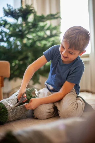 少年は自宅のリビングルームで人工的なクリスマスツリーを収集します — ストック写真