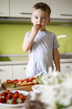 Neşeli çocuk mutfakta avokado, süzme peynir, meyve ve böğürtlenli sağlıklı kahvaltı hazırlıyor.