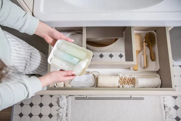 Manos de ama de casa poniendo toalla enrollada en el cajón debajo del fregadero. Organizar el espacio de almacenamiento en el baño —  Fotos de Stock