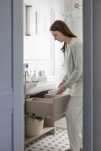 Dłonie gospodyni domowej wkładają zwinięty ręcznik do szuflady pod zlewem. Organizacja powierzchni magazynowej w łazience — Zdjęcie stockowe