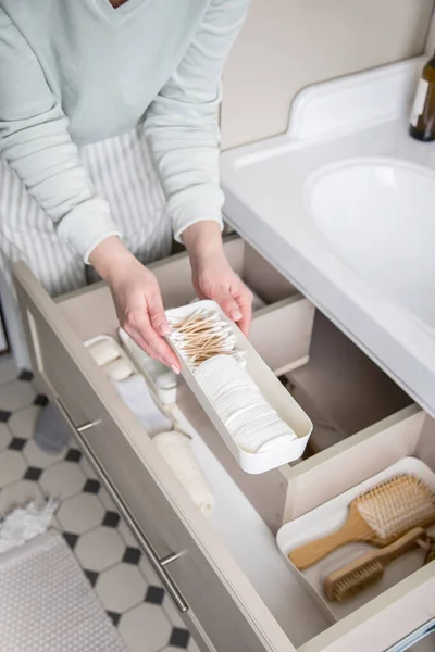 Ibu rumah tangga meletakkan handuk digulung ke dalam laci di bawah wastafel. Mengatur ruang penyimpanan di kamar mandi — Stok Foto