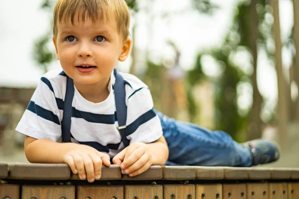 Крупним планом милий хлопчик лежить на дерев'яній лавці в парку розваг, розслабляючи літні канікули — стокове фото