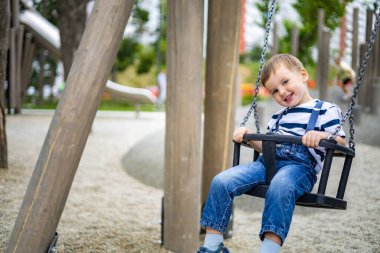 Eğlence parkında salıncakta sallanan gülümseyen çocuk ya da çocuk parkında olumlu duygular besleyen çocuk.