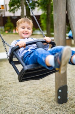 Eğlence parkında salıncakta sallanan gülümseyen çocuk ya da çocuk parkında olumlu duygular besleyen çocuk.