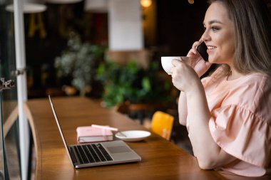 Düşünceli, zarif ve cüsseli bir iş kadını kahve içiyor kafede çalışıyor dizüstü bilgisayar kullanıyor ve tatilin tadını çıkarıyor.