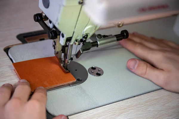 Close up craftsman hands sew stuff blank for wallet use sewing machine. Working at leather workshop