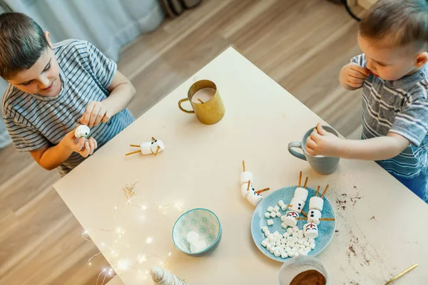 아이들은 마시멜로와 가죽끈으로 눈 사람을 만들고, 부엌에서 코코아를 마신다. 크리스마스와 새해를 위한 준비. — 스톡 사진