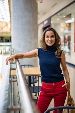 Alışveriş merkezinde poz veren ve hafta sonunun tadını çıkaran mutlu, şık genç bir kadının portresi.