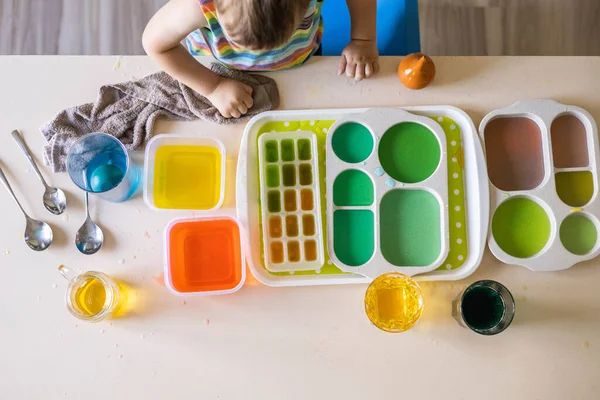Lindo bebé aprendiendo mezclando diferentes colores con agua y pintura en recipientes. Desarrollo temprano — Foto de Stock