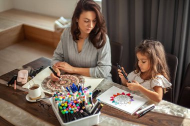Genç, güzel anne ve tatlı kız birlikte bir mandala deseni çiziyorlar. Sanatsal kalemler ve renkli kalemler..
