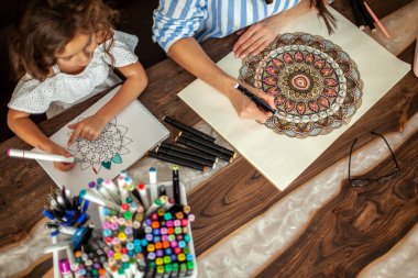 Genç, güzel anne ve tatlı kız birlikte bir mandala deseni çiziyorlar. Sanatsal kalemler ve renkli kalemler..