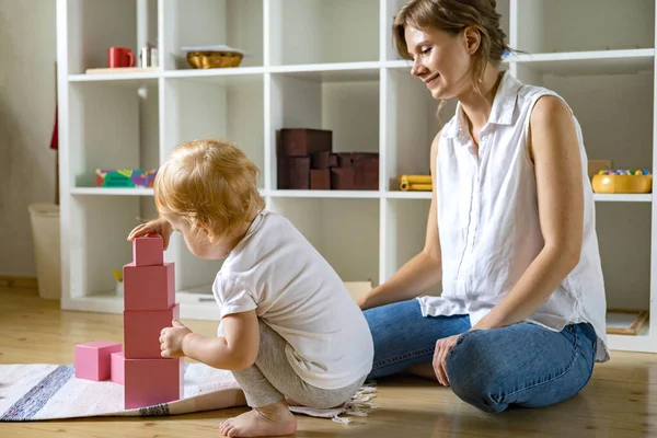 Madre joven y bebé pequeño ensamblando cubo rosa Maria Montessori materiales ecológicos —  Fotos de Stock