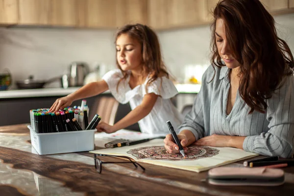 Genç, güzel anne ve tatlı kız birlikte bir mandala deseni çiziyorlar. Sanatsal kalemler ve renkli kalemler..
