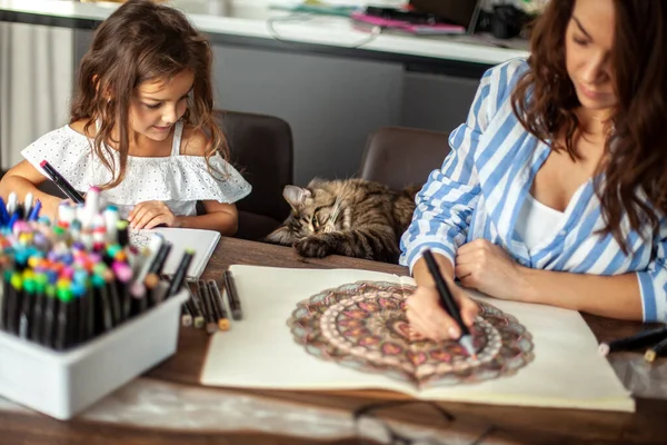 Genç, güzel anne ve tatlı kız birlikte bir mandala deseni çiziyorlar. Sanatsal kalemler ve renkli kalemler..