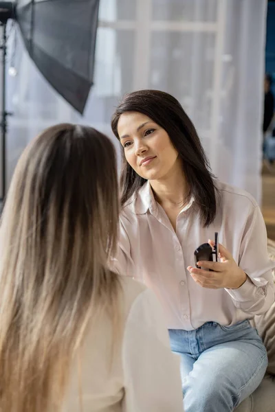 Maquiador feminino profissional aplicando cosméticos no rosto de modelo usa  escova trabalhando no salão de beleza. mulher visagista maquilagem mestre  tingimento de rosto para reforma da aparência do cliente