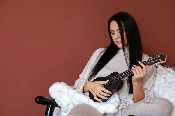 Mulher bonita feliz músico tocando no ukulele escrevendo música sentada no sofá confortável em casa — Fotografia de Stock