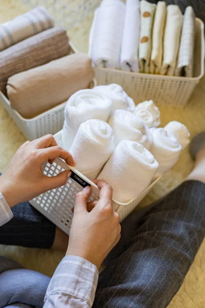 Vrouw handen netjes gevouwen linnengoed en handdoeken gebruik Marie Kondo methode met kleverige label tags — Stockfoto
