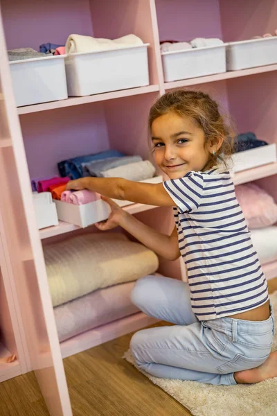 Vista superior niña cuidadosamente doblado ropa en la caja de la caja para el almacenamiento vertical cómodo en los estantes —  Fotos de Stock