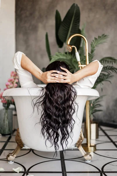 Volver ver moda rizado morena mujer acostada en baño con agua relajante disfrutando de procedimiento de spa —  Fotos de Stock