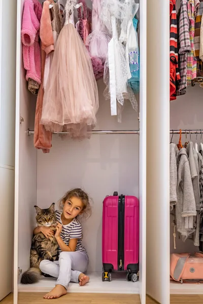 Забавная маленькая девочка прячется в шкафу обнимая кота чувствуя любовь и позитивные эмоции — стоковое фото