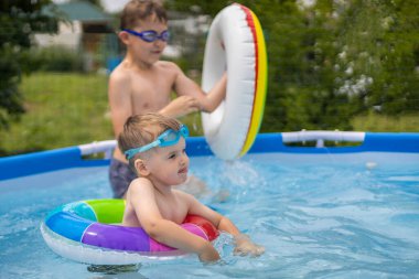 Evin yakınındaki açık havuzda yüzen ve oynayan iki erkek kardeş. Renkli, yüzen, parlak, gökkuşağı daireleri.