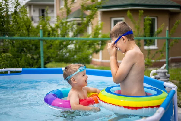 Evin yakınındaki açık havuzda yüzen ve oynayan iki erkek kardeş. Renkli, yüzen, parlak, gökkuşağı daireleri. — Stok fotoğraf