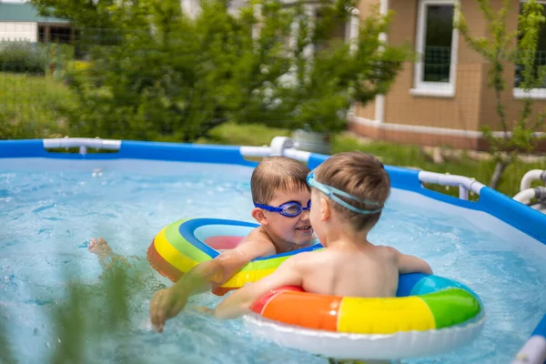Two boys brothers in the outdoor outdoor pool near the house swim and play. Colored, swimming, bright, rainbow circles. — Stock Photo, Image