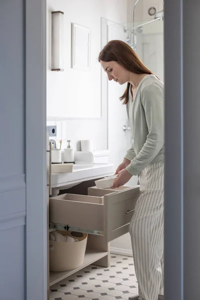 Dłonie gospodyni domowej wkładają zwinięty ręcznik do szuflady pod zlewem. Organizacja powierzchni magazynowej w łazience — Zdjęcie stockowe