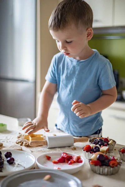 Vrolijke mannelijke baby koken zelfgemaakte zomer dessert met fruit en bessen thuis keuken Stockfoto