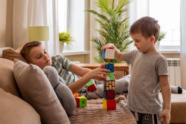 Farklı Rubiks küplerinden kule inşa eden komik erkek çocuklar evdeki kanepede birlikte oynuyorlar.